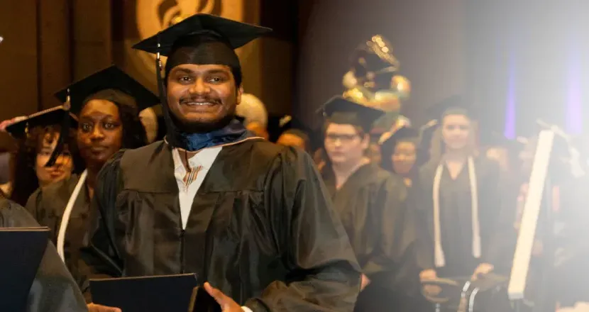 Herzing University online MBA graduate smiling while walking to receive his degree